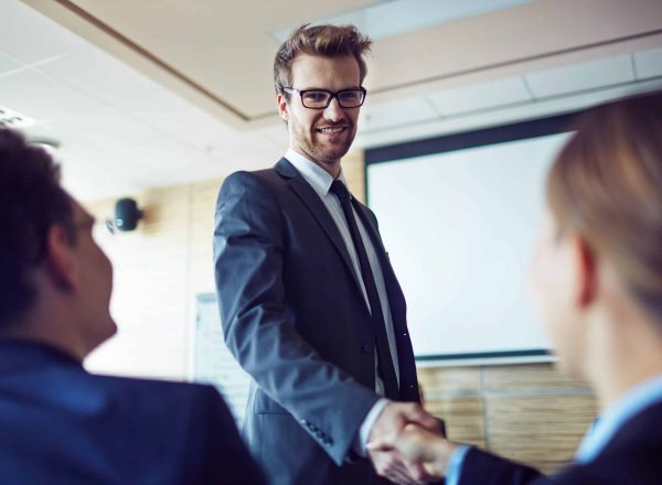 Elegant employee in suit and eyeglasses greeting businesswoman at conference