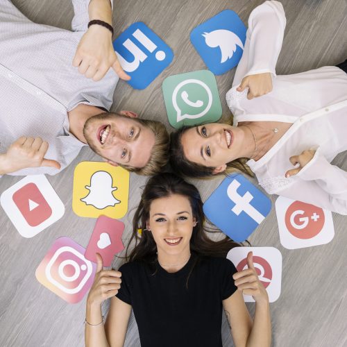 young-smiling-friend-lying-floor-with-social-media-logos-showing-thumbup-sign-scaled